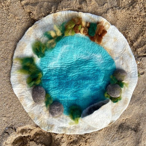 Rockpool, a round felt mat with a turquoise pool at its center, ringed by felt rocks, seaweed and a sandy shore