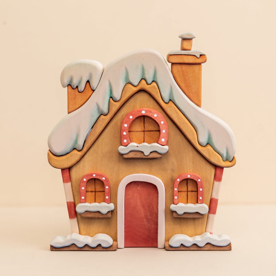 Wooden Christmas house with a snow-covered roof, a red door, and lit windows