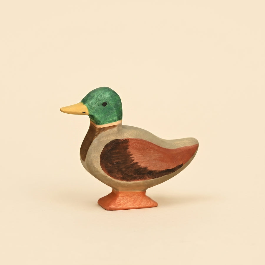 Wooden mallard duck figure with a green head, yellow bill, and chestnut wing, standing on an orange base