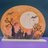 Wooden Halloween scene panel with a full moon, bats, and bare trees cut through the wood, on a standing base · view 1