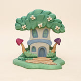 Wooden fairy house grown into a flowering tree, on a carved base with a stone path and toadstools · view 1