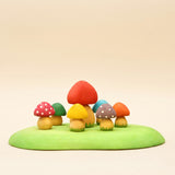 Set of small wooden mushrooms in red, yellow, and orange on a green base · view 1