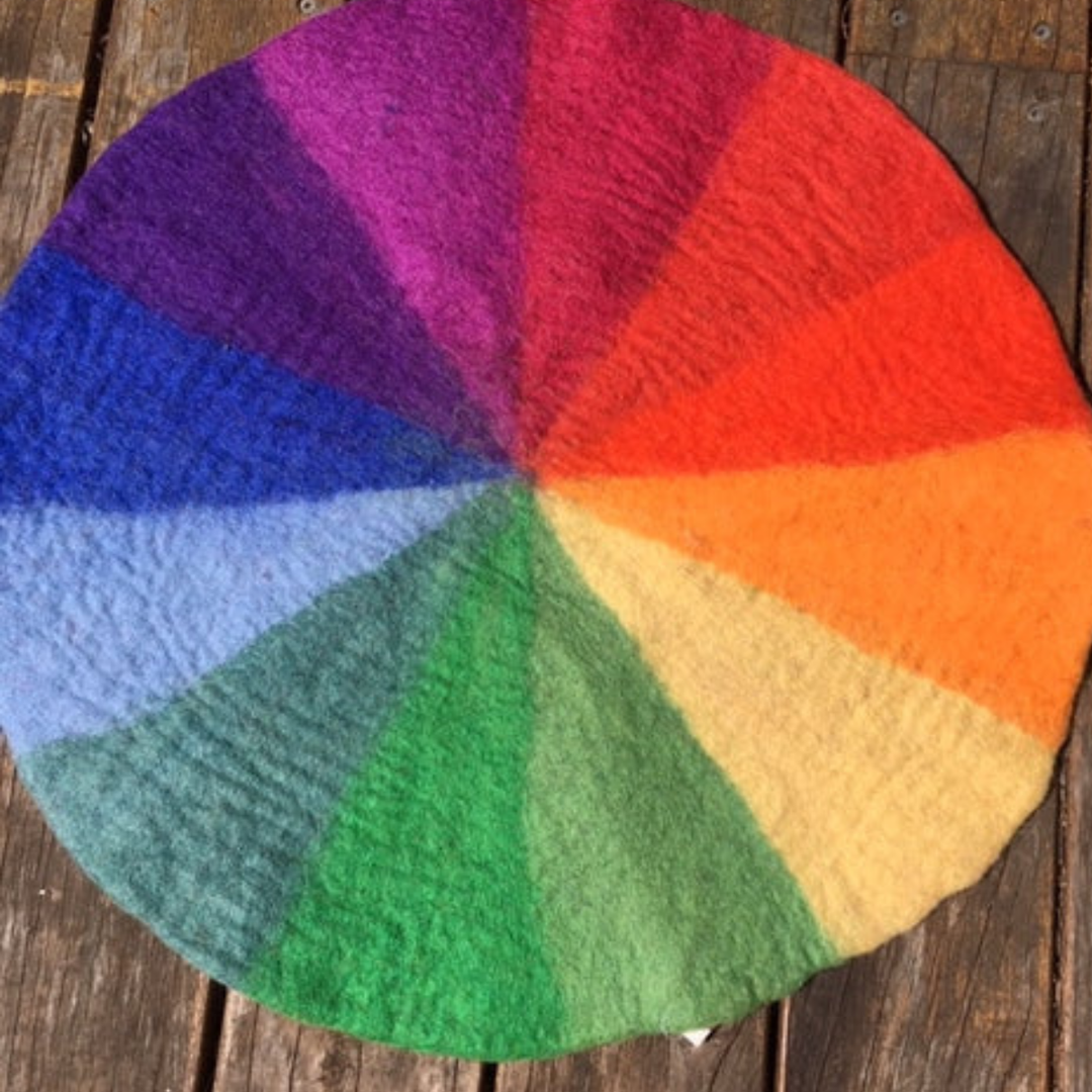 Papoose Goethe Colour Wheel Felt Play Mat — a reversible hand-felted wool mat with twelve pie-shaped Goethe-colour segments forming a full colour wheel on both sides, for colour sorting, seriation, and pattern play