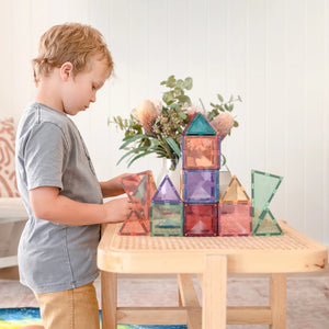 A child building a small tower from Pastel magnetic tiles at a rattan table