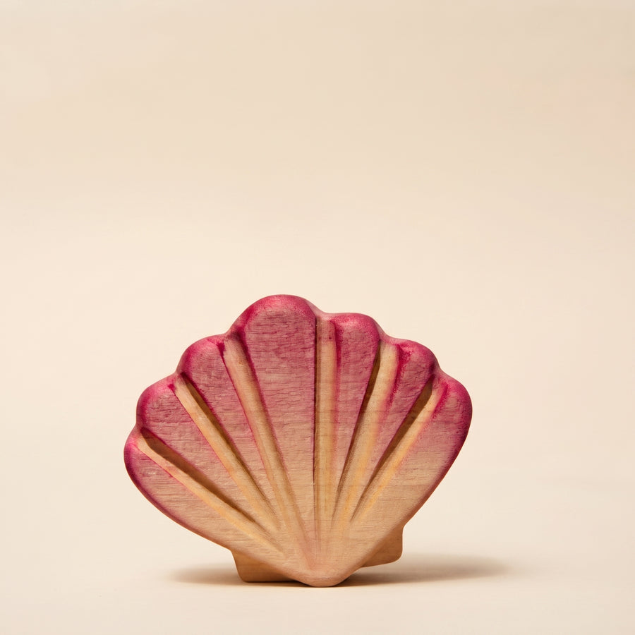 Wooden scallop shell painted pink, standing upright on sand