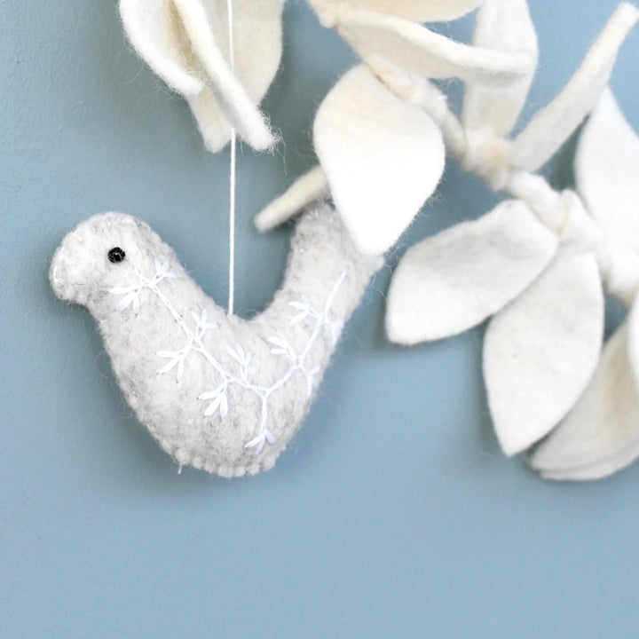 Close up of a grey felt dove with a white embroidered sprig and a small black bead eye, hanging from the cream leaf garland