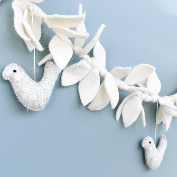 Felt doves and leaves garland strung along a wall, cream leaves knotted along a twisted cord with grey doves hanging below