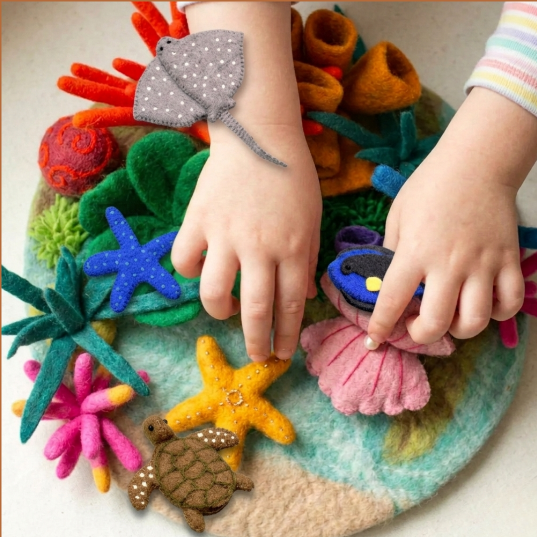 A child's hands place a starfish and tang fish in the Coralwhim Cove felt habitat with coral and a sea turtle.